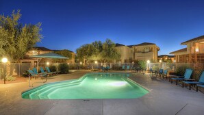 A swimming pool with lounge chairs and umbrellas, surrounded by buildings and trees. - Spacious condo with pools, hot tub, patio & lovely views - dog-friendly (Oro Valley)
