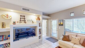 A living room with a TV, sofa, and a bookshelf. - Spacious condo with pools, hot tub, patio & lovely views - dog-friendly (Oro Valley)