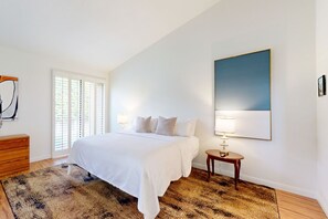 Ein Schlafzimmer mit einem großen Bett, einem Nachttisch, einer Lampe und einem Fenster mit Jalousien.