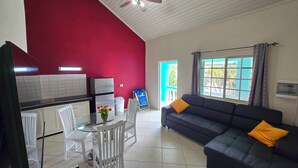 A compact living space with a kitchenette, a dining area with a glass table, and a sofa with cushions. - Adorable 1-bedroom Apartment 3 km From Eagle Beach (Noord)