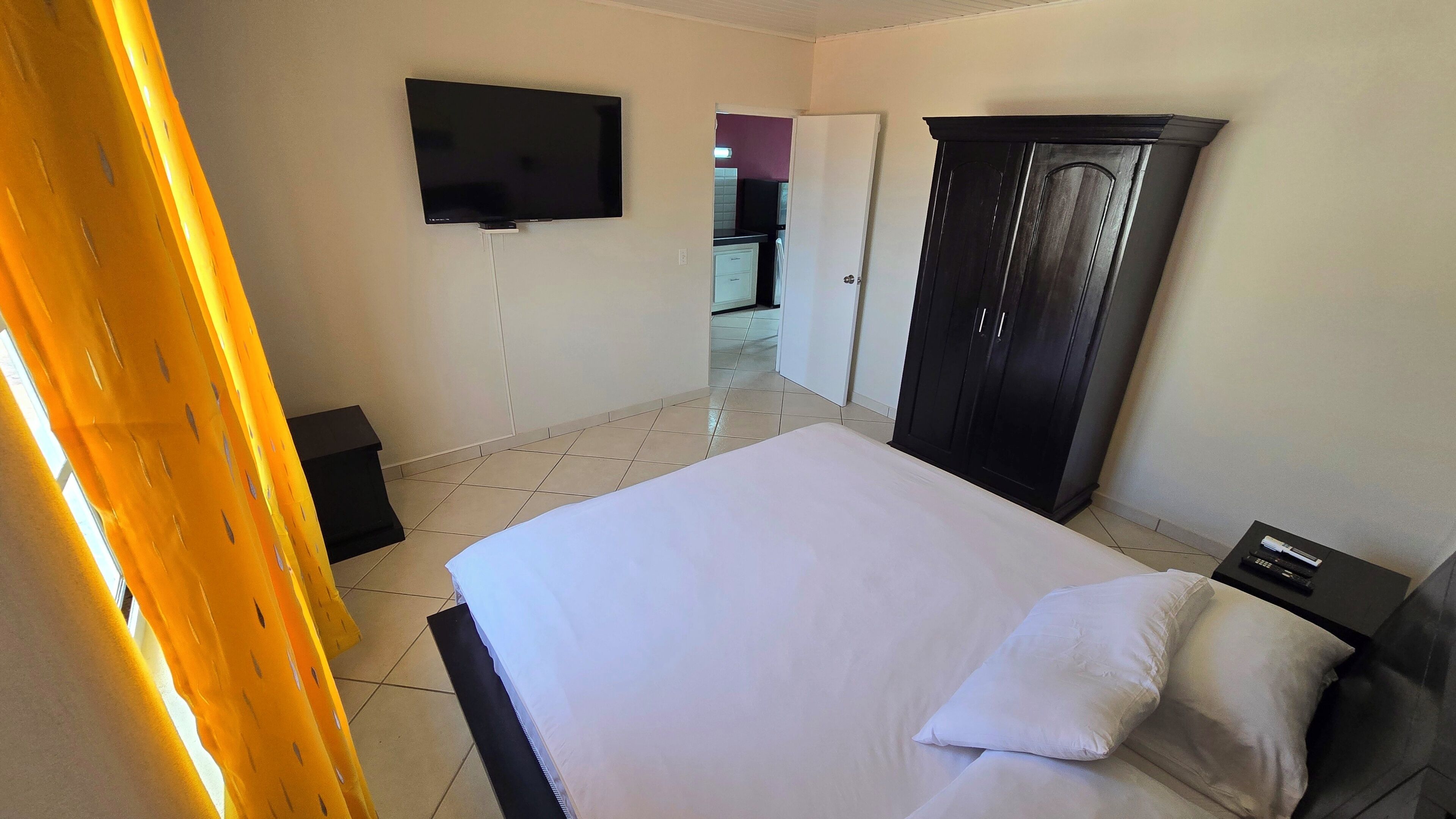 Habitación de hotel con cama, armario, televisor y baño visible a través de una puerta abierta.