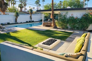 A backyard with a swimming pool, a covered seating area, and a well-maintained lawn. - Cheerful mid-century home w/ private pool, spa, firepit & mountain views (Palm Springs)