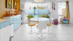 A bright kitchen with white cabinets, a dining area with white chairs, and a view of a pool outside. - Cheerful mid-century home w/ private pool, spa, firepit & mountain views (Palm Springs)