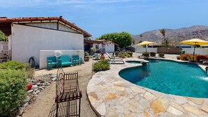 Ein Poolbereich mit Steinböden, Sitzgelegenheiten im Freien und Sonnenschirmen.
