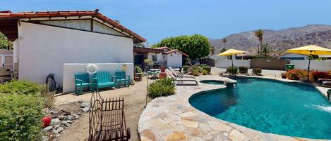 A pool area with stone flooring, outdoor seating, and umbrellas.