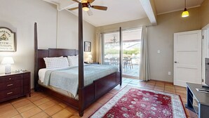 Ein Schlafzimmer mit Himmelbett, Deckenventilator, Teppich in Rot und Weiß sowie ein Nachttisch mit Lampe. Durch eine Schiebetür ist ein Blick ins Freie möglich.