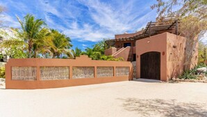 A sandy driveway leading to a building with a traditional design, a covered entrance, and a wall with woven panels. - 3 Bedroom with Pool & Mountain Views (Los Barriles)