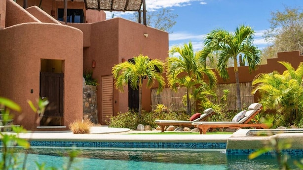 A resort with a swimming pool, palm trees, and a building with a unique architectural style. - 3 Bedroom with Pool & Mountain Views (Los Barriles)