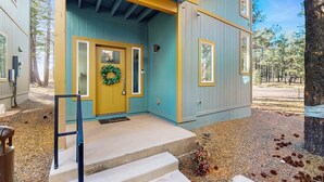 A building with a yellow door, a blue exterior, and a wooden porch. - Modern, dog-friendly bungalow home with patio, balcony, & central AC (Flagstaff)