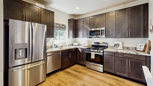 A modern kitchen with stainless steel appliances, dark wood cabinets, and a granite countertop. - Modern, dog-friendly bungalow home with patio, balcony, & central AC (Flagstaff)