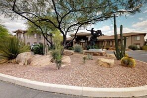 A residential area with a cactus garden, a statue, and a building with a tiled roof. - Comfy, updated condo with pool & hot tub - dog-friendly (Oro Valley)