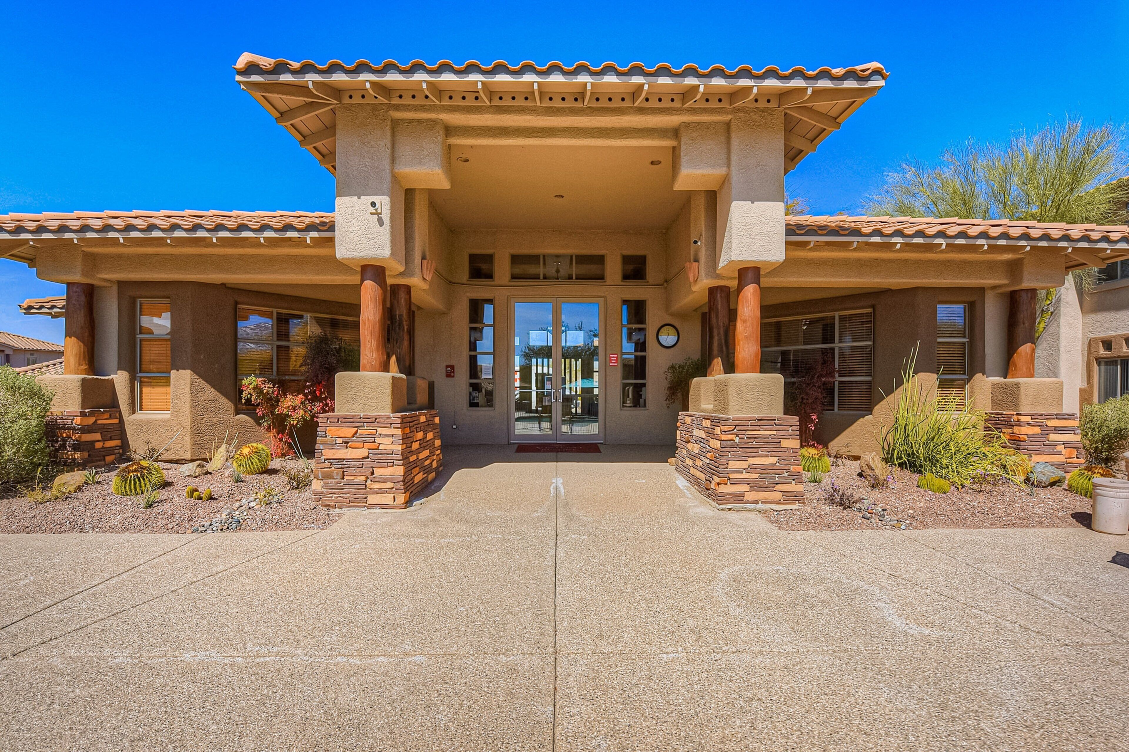 A two-story building with a tiled roof, a central entrance with glass doors, and a small garden with desert plants.
