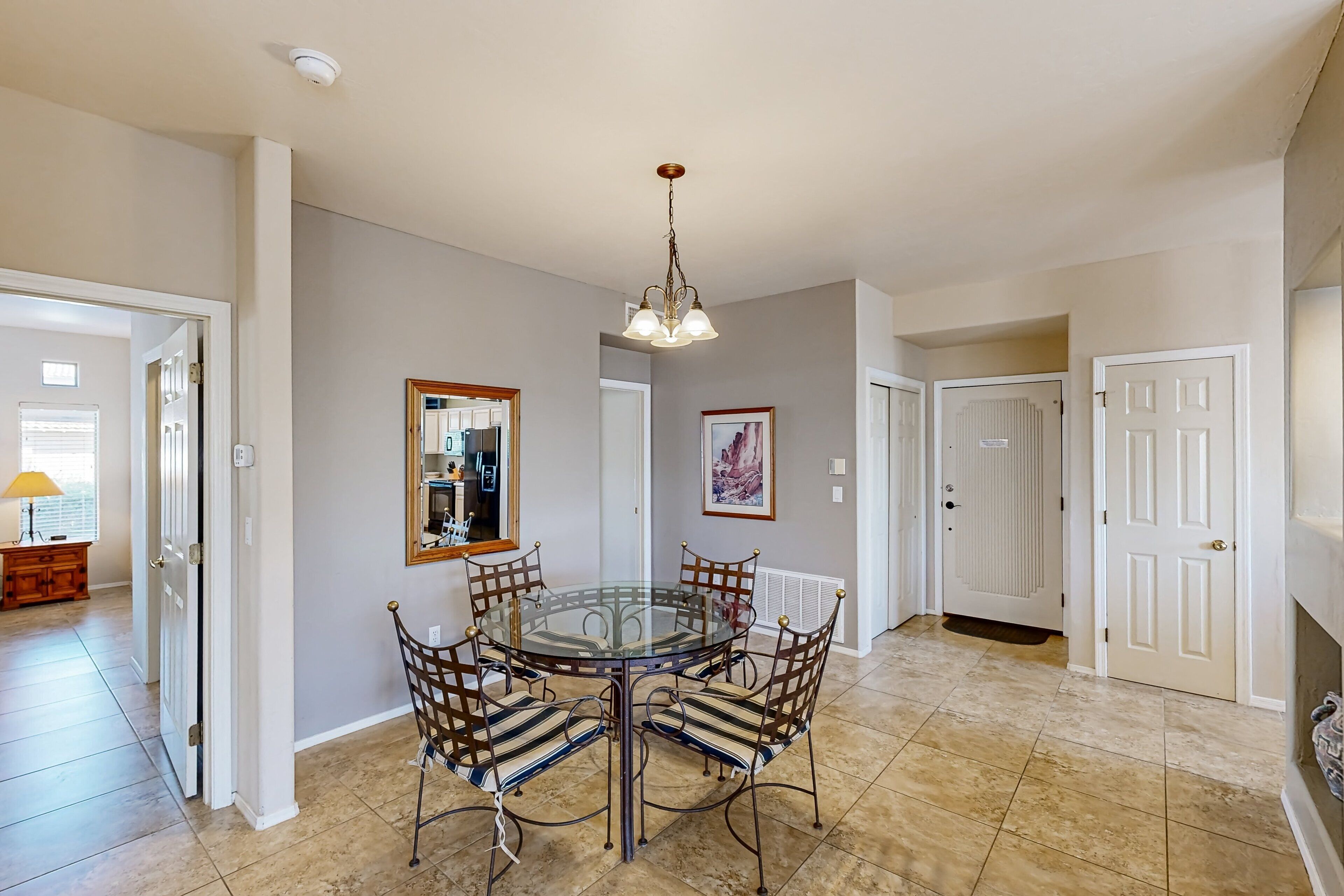 Uma sala de jantar com mesa de vidro rodeada por cadeiras de metal, um candelabro e um quadro na parede.