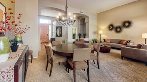 A spacious living room with a round dining table surrounded by chairs, a sofa, and a coffee table.