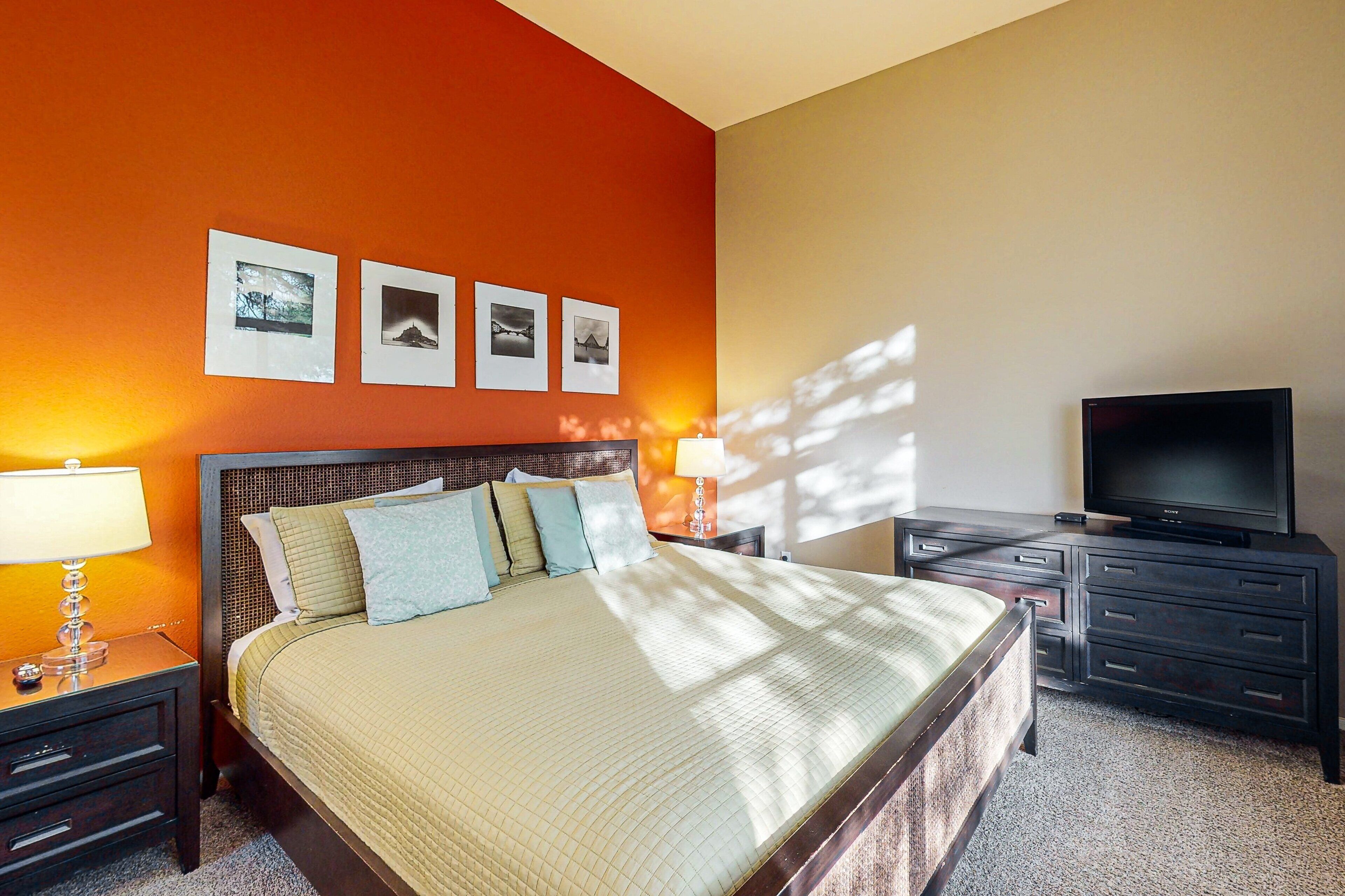 A hotel room with a bed, bedside tables, a TV, and framed pictures on the wall.