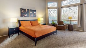 A bedroom with a bed, two bedside tables, a chair, a window with curtains, and artwork on the wall.