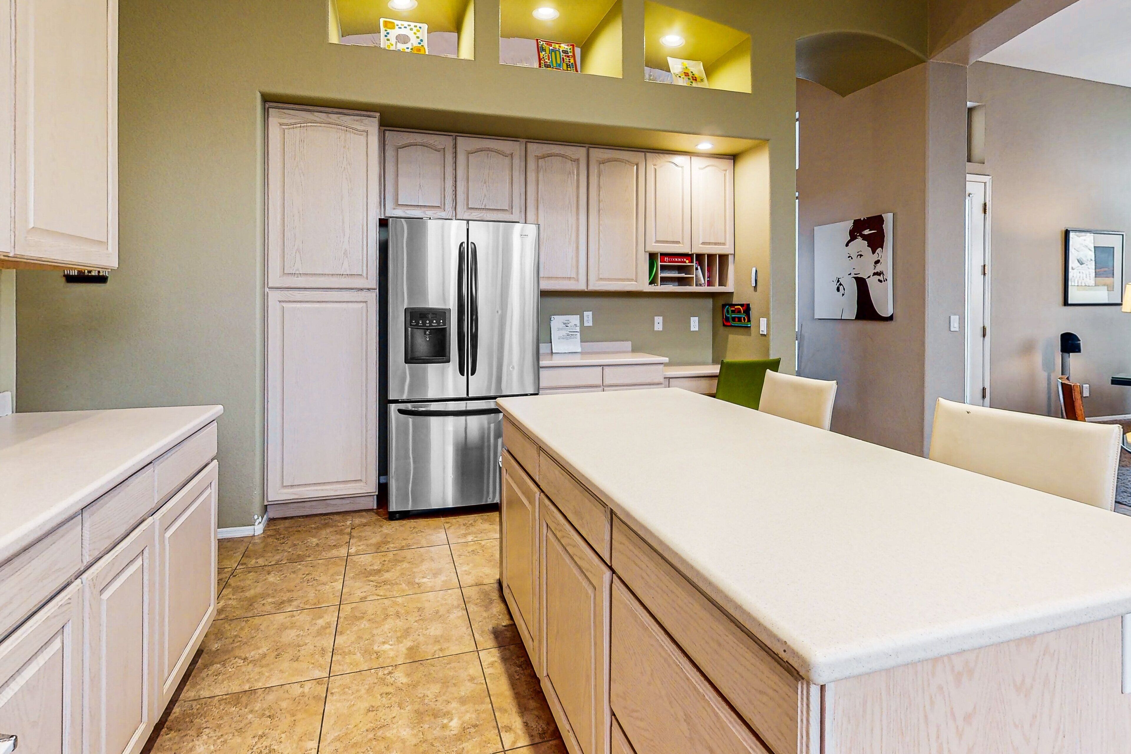 A kitchen with a stainless steel refrigerator, wooden cabinets, and a large island.