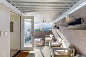 A balcony with a seating area, a door leading outside, and a view of buildings and mountains. - Stunning luxury home w/pool, spa, outdoor fireplace & mountain views (Palm Springs)