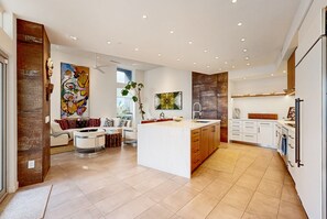 A modern kitchen with a central island, white cabinetry, and a large window. - Stunning luxury home w/pool, spa, outdoor fireplace & mountain views (Palm Springs)