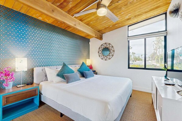 A bedroom with a bed, a desk, a ceiling fan, a window, and a patterned wall. - Mid-century oasis w/ circular heated pool, hot tub, & stunning mountain views (Palm Springs)