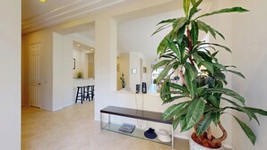 Un intérieur moderne avec une table à plateau de verre, une plante en pot et un coin cuisine à l’arrière-plan.