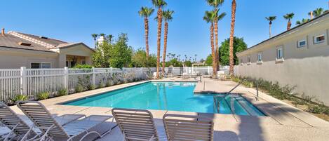 A swimming pool with lounge chairs, palm trees, and a white fence.