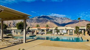 Ein Poolbereich mit Liegestühlen, einer überdachten Lounge und Blick auf die Berge.