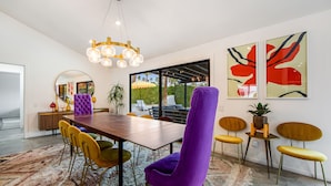 Uma sala de jantar moderna com uma mesa de madeira, cadeiras roxas e amarelas, e um candelabro.