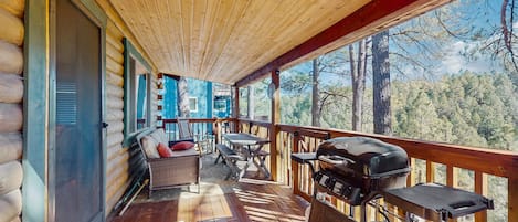 A wooden deck with a grill, seating area, and a view of the forest.
