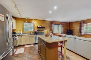 A compact kitchen with wooden walls, a built-in refrigerator, and a dining area with a wooden table and chairs. - Cabin with grill, outdoor dining, & fireplace - drive minutes to hiking (Flagstaff)