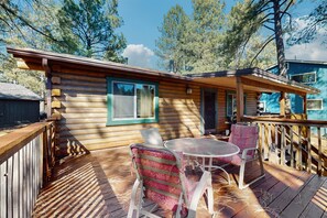 Une cabane en bois avec une terrasse, deux chaises et une table.