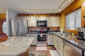 A modern kitchen with stainless steel appliances, granite countertops, wooden cabinets, and a large window with blinds. - Cabin with grill, outdoor dining, & fireplace - drive minutes to hiking (Flagstaff)