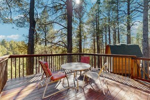 Une terrasse en bois avec une table et des chaises, entourée de grands arbres.