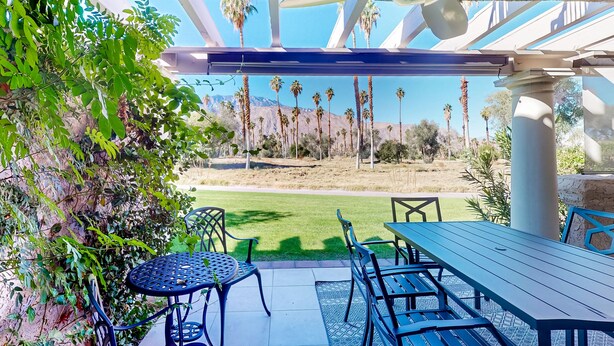 An outdoor patio with a table and chairs, a pergola overhead, and a view of palm trees and mountains. - Modern palm-surrounded condo with mtn views, heated pool, & AC - dog-friendly (Palm Springs)