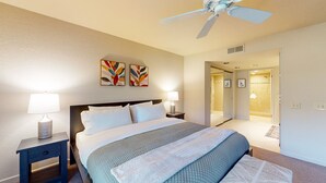 A hotel room with a bed, two bedside lamps, a ceiling fan, and a door leading to a bathroom. - Modern palm-surrounded condo with mtn views, heated pool, & AC - dog-friendly (Palm Springs)
