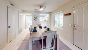 A dining area with a long table set for six, a ceiling fan, and a view into the kitchen. - Modern palm-surrounded condo with mtn views, heated pool, & AC - dog-friendly (Palm Springs)