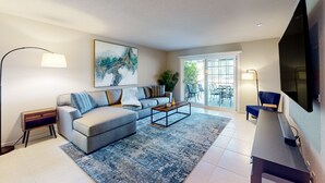 A modern living room with a grey sofa, a coffee table, and a flat-screen TV. - Modern palm-surrounded condo with mtn views, heated pool, & AC - dog-friendly (Palm Springs)