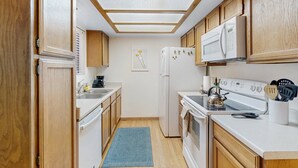 Una cocina compacta con armarios de madera, un refrigerador blanco, una estufa y un microondas.