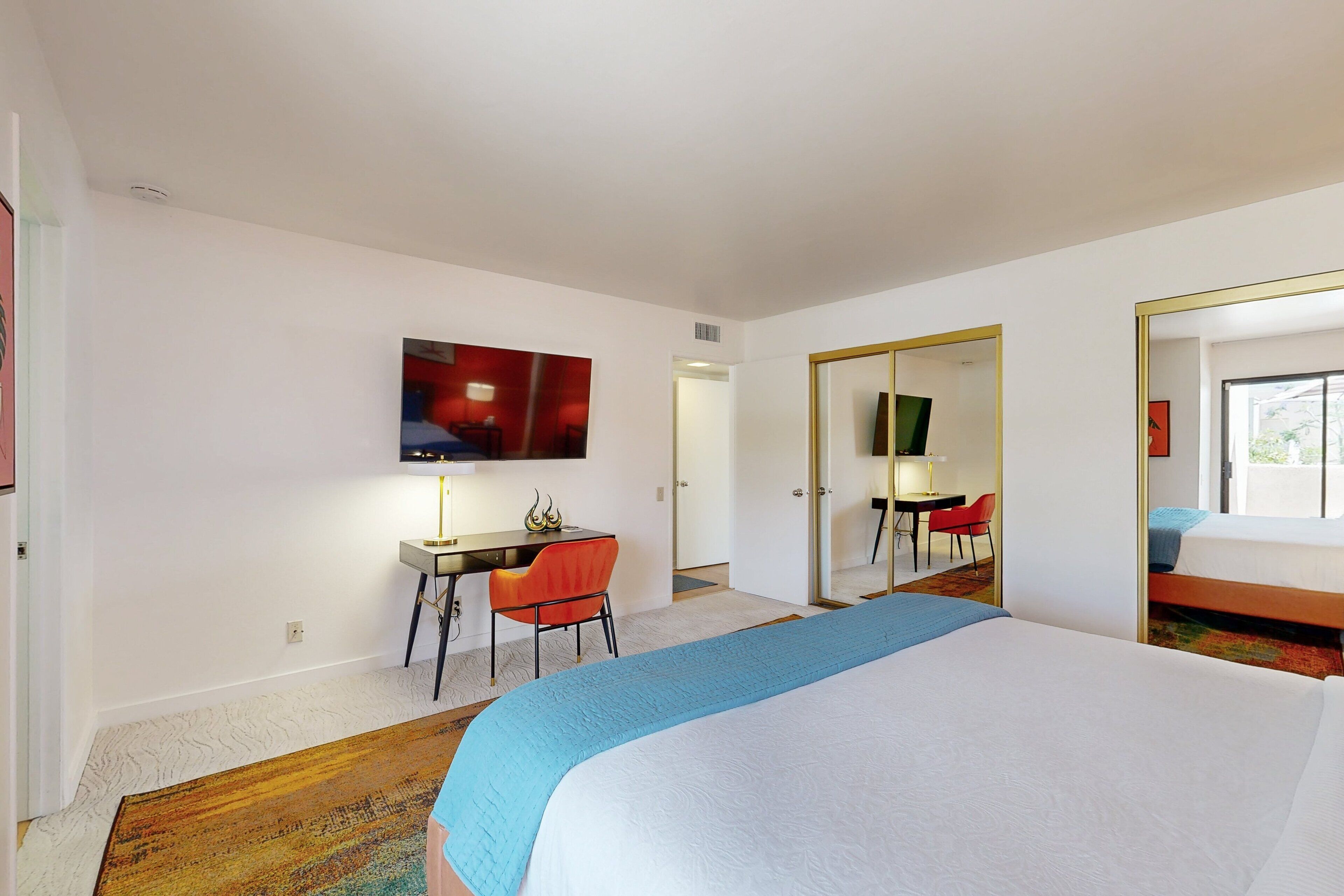 A hotel room with a large bed, a desk with a chair, a television, and a mirror.