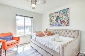 A bedroom with a large bed, a tufted headboard, a colorful abstract painting, a window, and a modern orange chair.