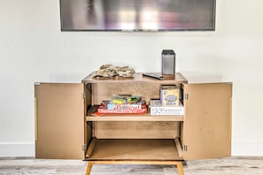 Ein kleiner Holzschrank mit einem darüber angebrachten Fernseher, einer Fernbedienung und Brettspielen auf den Regalen.