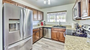 A kitchen with stainless steel appliances, wooden cabinets, granite countertops, and a window providing natural light. - Single-level dog-friendly home with private pool, grill, enclosed backyard, & AC (Chandler)