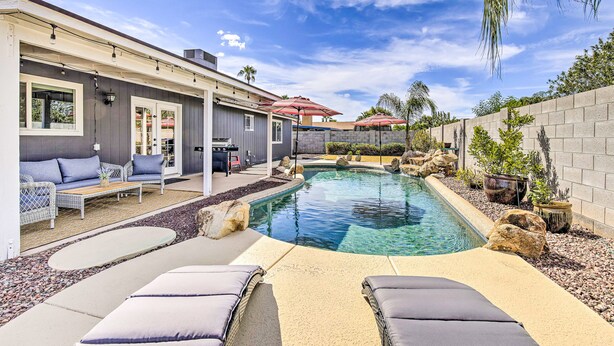 A backyard with a swimming pool, lounge chairs, a barbecue area, and a stone wall. - Single-level dog-friendly home with private pool, grill, enclosed backyard, & AC (Chandler)