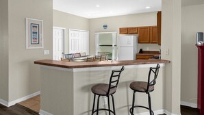 A kitchen with a central island, wooden cabinets, a refrigerator, and a dining area with chairs. - Gorgeous Executive Disney Pool Home in High Grove Clermont 4BR/ 3BA (Clermont)