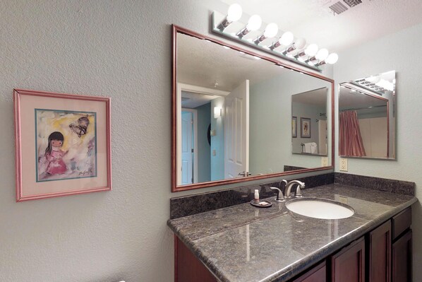 A bathroom with a large mirror, vanity, and a framed picture on the wall. - Modern condo near golf with a shared pool, hot tub (Tucson)