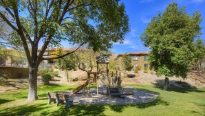 Une aire de jeux avec un toboggan et des structures d’escalade, entourée d’arbres et d’une pelouse.