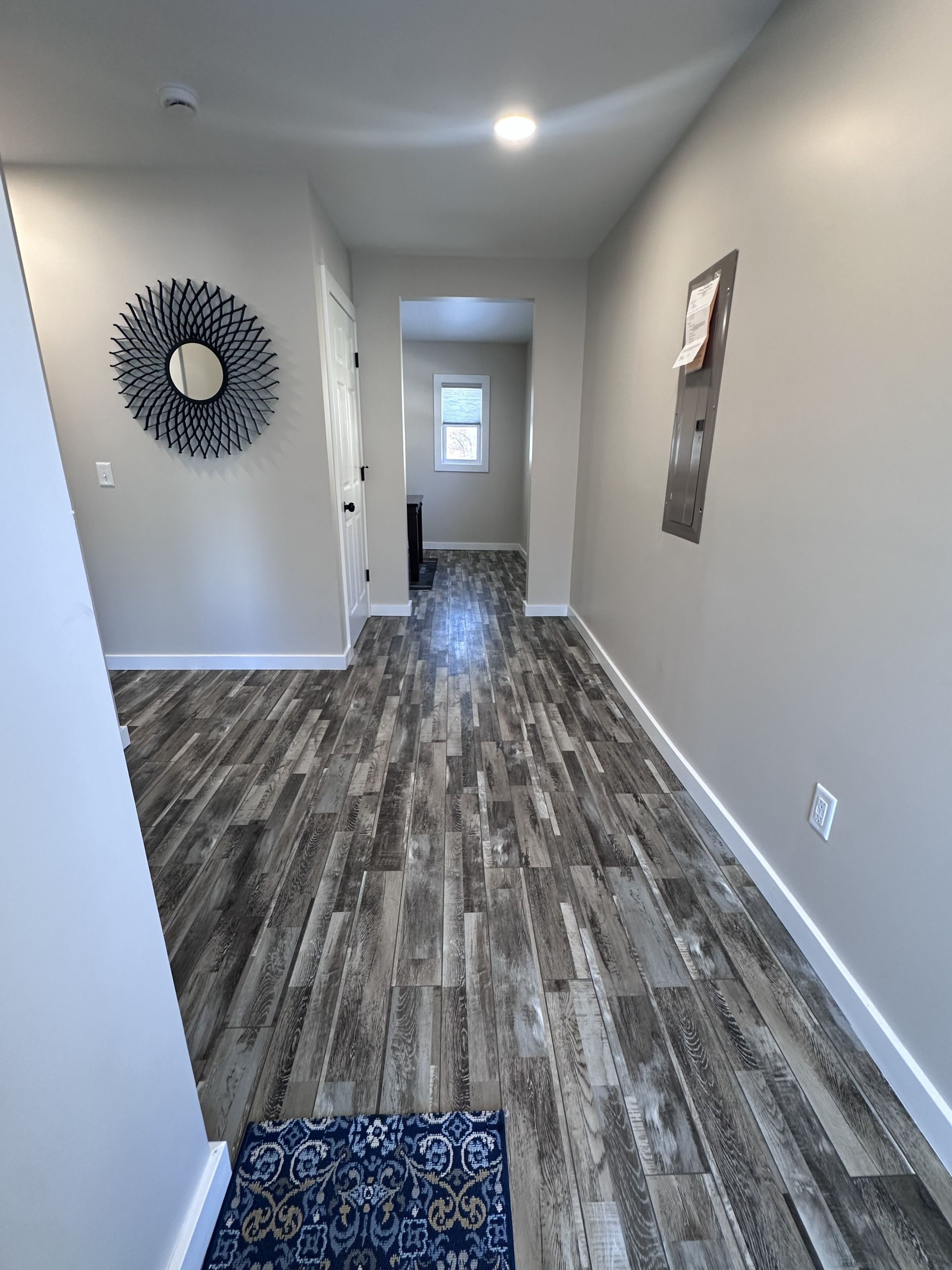 A hallway with wooden flooring, a decorative mirror, and a small rug.