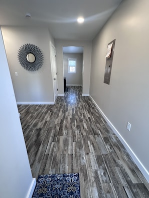 A hallway with wooden flooring, a decorative mirror, and a small rug. - State Street Retreat (Big Rapids)