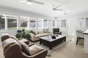 Un salon spacieux avec un canapé beige, deux fauteuils, une table basse et un coin repas agrémenté d’un buffet blanc.