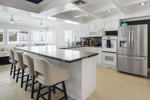 A modern kitchen with a large island, bar stools, stainless steel appliances, and white cabinetry. - Sunshine, Style & Your Own Private Pool Retreat – Dog-Friendly!- #112181 (La Quinta)